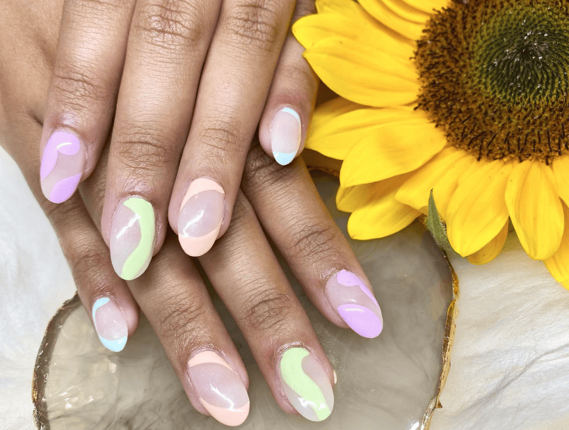 Hands with pastel swirl nail art rest near a sunflower on a marble surface.